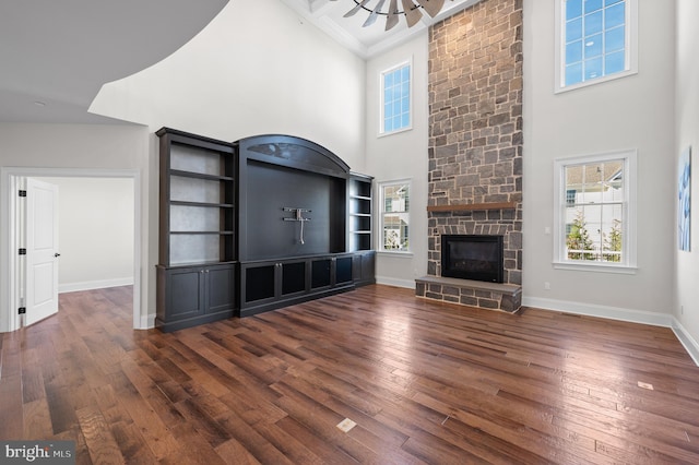 unfurnished living room with a towering ceiling, a stone fireplace, dark hardwood / wood-style flooring, and ornamental molding