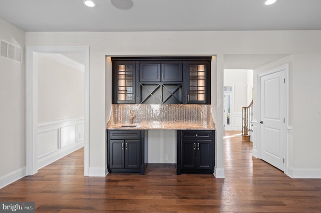 bar featuring dark wood-type flooring, tasteful backsplash, light stone countertops, and sink