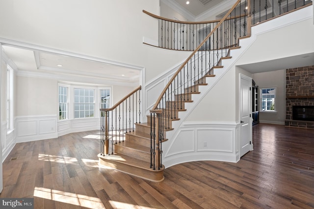 stairs featuring hardwood / wood-style flooring, a stone fireplace, a towering ceiling, and crown molding