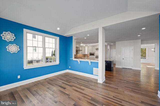 kitchen featuring lofted ceiling, dark wood-type flooring, white cabinets, kitchen peninsula, and a breakfast bar area