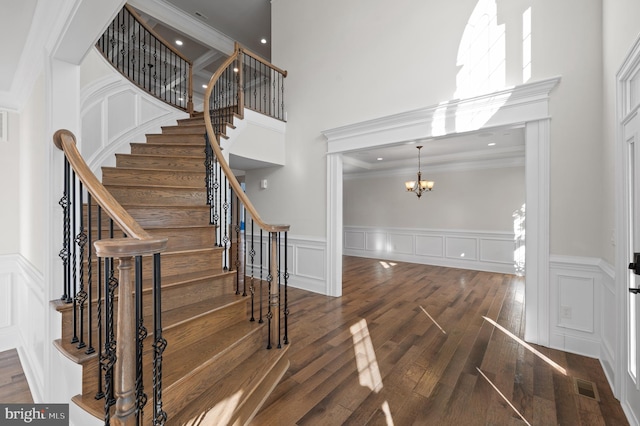 stairway with ornamental molding, hardwood / wood-style floors, a chandelier, and a high ceiling