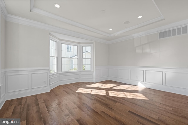 empty room with hardwood / wood-style flooring, a raised ceiling, and crown molding