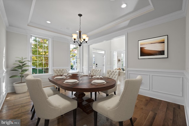 dining room with dark wood-type flooring, a chandelier, a raised ceiling, and crown molding