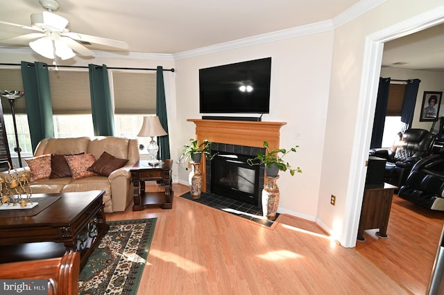 living room featuring crown molding, a tile fireplace, light wood-type flooring, and ceiling fan