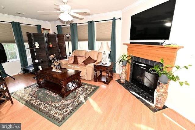 living room with ornamental molding, hardwood / wood-style floors, a tile fireplace, and ceiling fan