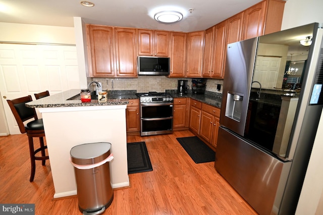 kitchen featuring appliances with stainless steel finishes, a breakfast bar area, dark stone counters, decorative backsplash, and light hardwood / wood-style flooring