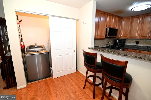 kitchen featuring washer / clothes dryer, light wood-type flooring, backsplash, dark stone countertops, and a breakfast bar