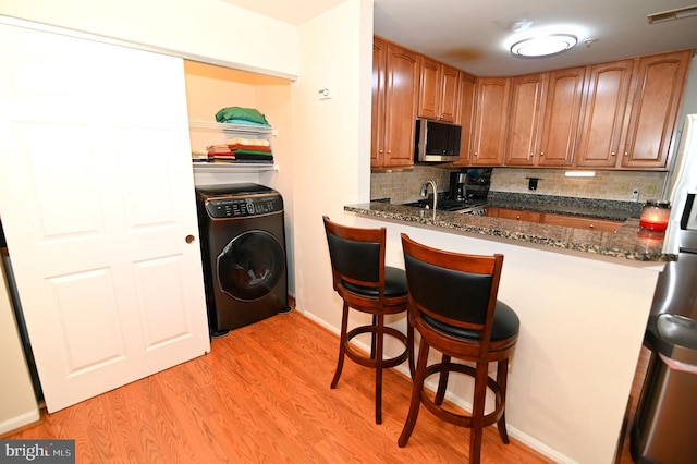 kitchen with washer / dryer, tasteful backsplash, appliances with stainless steel finishes, dark stone countertops, and light hardwood / wood-style floors