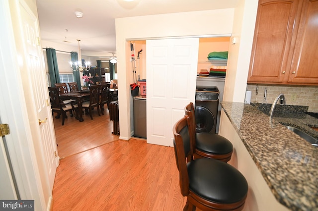 kitchen featuring tasteful backsplash, dark stone counters, pendant lighting, light hardwood / wood-style floors, and sink