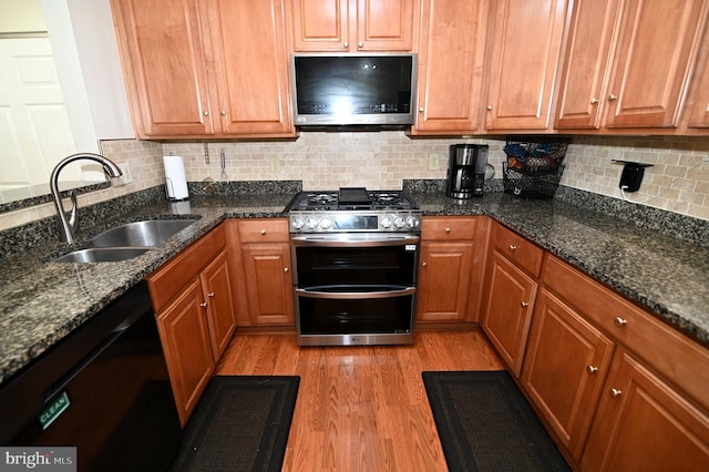 kitchen with stainless steel appliances, backsplash, dark stone counters, sink, and light wood-type flooring