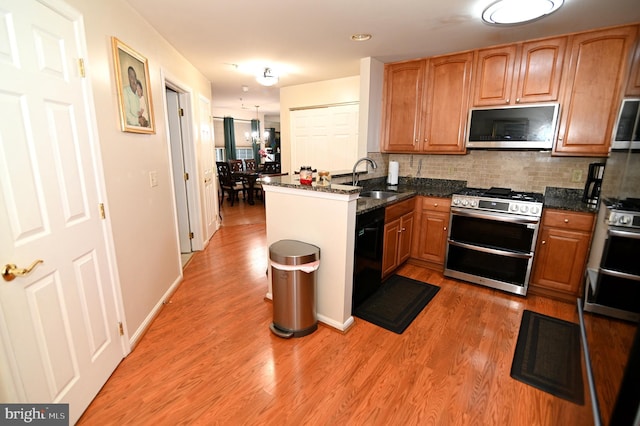 kitchen with kitchen peninsula, appliances with stainless steel finishes, hardwood / wood-style flooring, dark stone counters, and sink