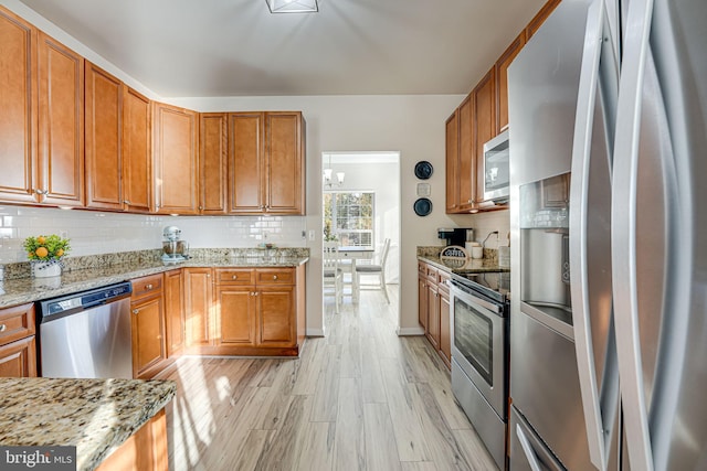 kitchen with light hardwood / wood-style floors, tasteful backsplash, stainless steel appliances, and light stone counters