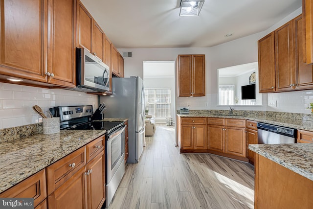 kitchen featuring sink, light stone countertops, light wood-type flooring, appliances with stainless steel finishes, and tasteful backsplash