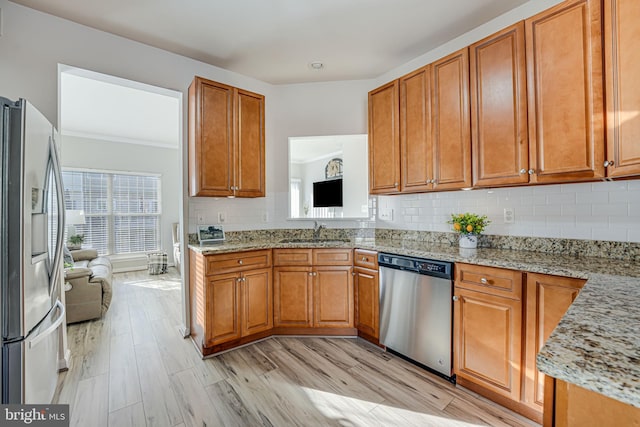 kitchen with appliances with stainless steel finishes, sink, light wood-type flooring, and light stone counters