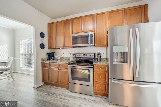 kitchen with appliances with stainless steel finishes, decorative backsplash, light stone countertops, and light hardwood / wood-style floors