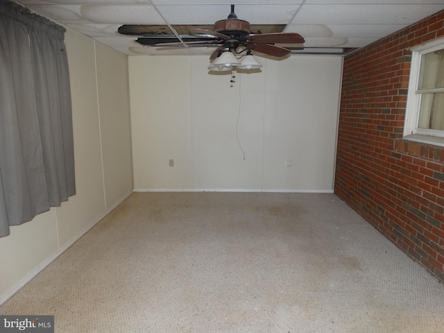 carpeted empty room featuring brick wall, a paneled ceiling, and ceiling fan