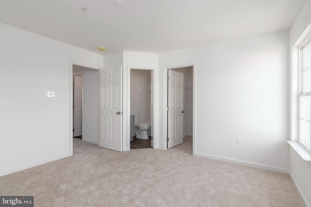 unfurnished bedroom with a walk in closet, ensuite bathroom, and light colored carpet