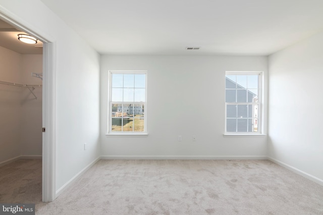 unfurnished bedroom featuring a spacious closet, multiple windows, a closet, and light colored carpet