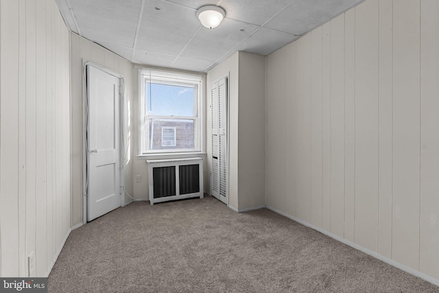 carpeted spare room with wooden walls and radiator