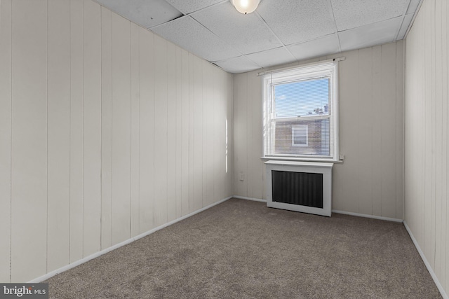 carpeted spare room featuring radiator, a drop ceiling, and wooden walls