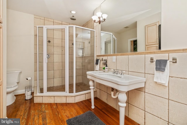 bathroom with hardwood / wood-style flooring, toilet, tile walls, a chandelier, and walk in shower