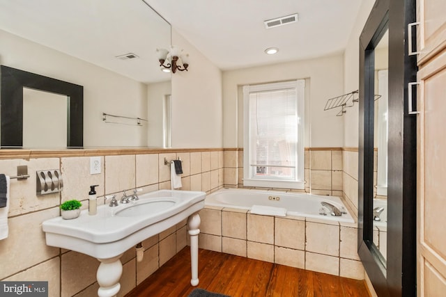 bathroom with a relaxing tiled tub and hardwood / wood-style flooring