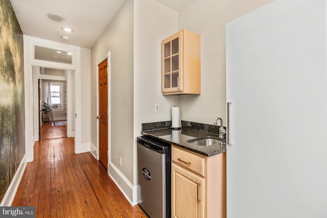 kitchen with hardwood / wood-style floors, stainless steel dishwasher, light brown cabinetry, dark stone countertops, and sink