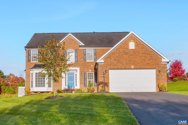 colonial-style house with driveway, brick siding, an attached garage, and a front yard