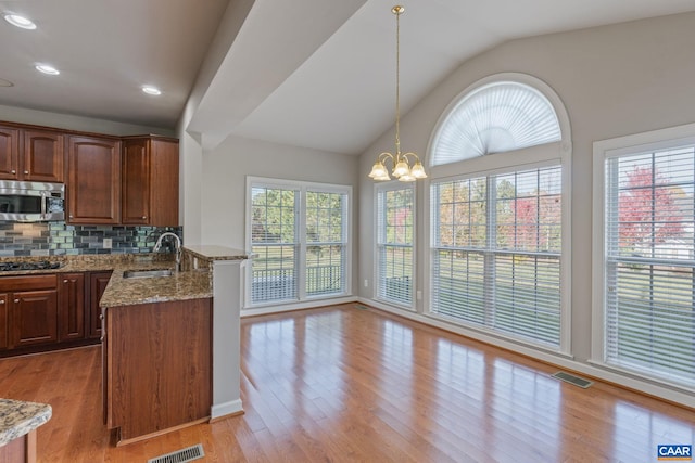 kitchen with stone counters, a notable chandelier, stainless steel microwave, a sink, and light wood-type flooring