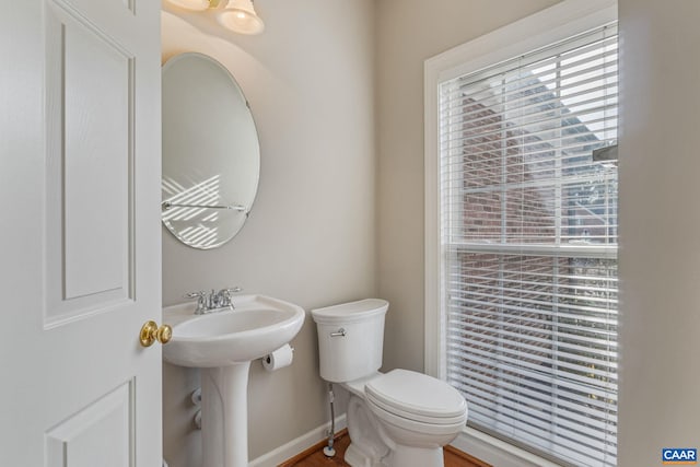 half bath featuring toilet, baseboards, and a sink