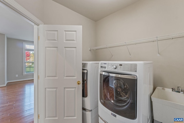 laundry room featuring washing machine and clothes dryer, a sink, wood finished floors, laundry area, and baseboards