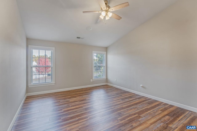 spare room featuring lofted ceiling, dark wood-style flooring, a ceiling fan, visible vents, and baseboards