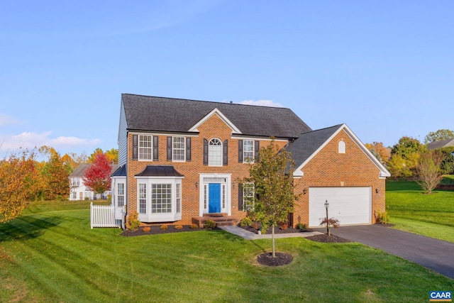 colonial inspired home featuring aphalt driveway, an attached garage, brick siding, a shingled roof, and a front lawn