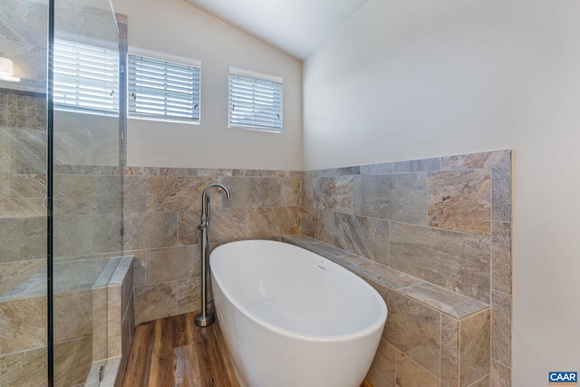 full bath featuring a wainscoted wall, tile walls, vaulted ceiling, wood finished floors, and a freestanding tub