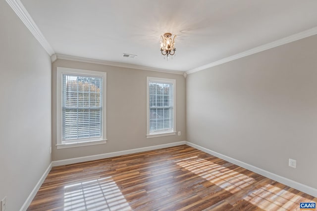 spare room with crown molding, visible vents, an inviting chandelier, wood finished floors, and baseboards