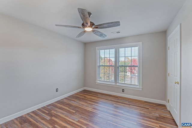 unfurnished room with a ceiling fan, visible vents, baseboards, and wood finished floors