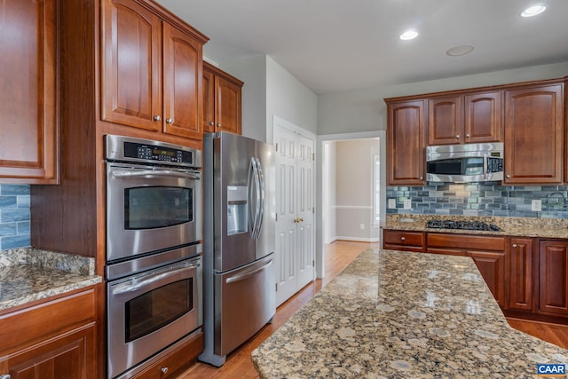 kitchen featuring light wood-style floors, appliances with stainless steel finishes, backsplash, and light stone counters