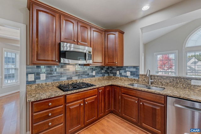 kitchen featuring appliances with stainless steel finishes, backsplash, a sink, and light stone countertops