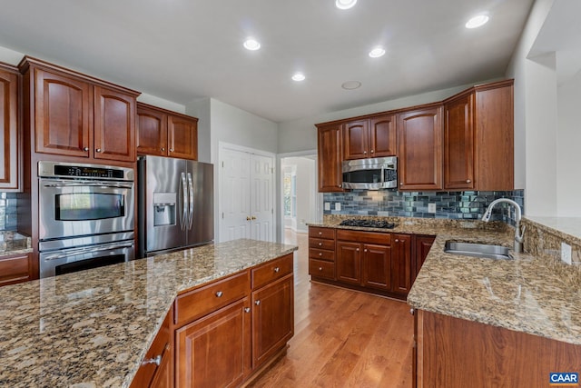 kitchen with light wood finished floors, decorative backsplash, light stone countertops, stainless steel appliances, and a sink