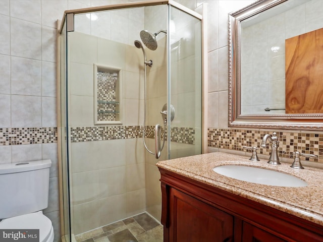 bathroom featuring a shower with door, toilet, tile walls, vanity, and decorative backsplash