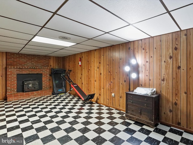 workout area with wooden walls, a drop ceiling, and a wood stove