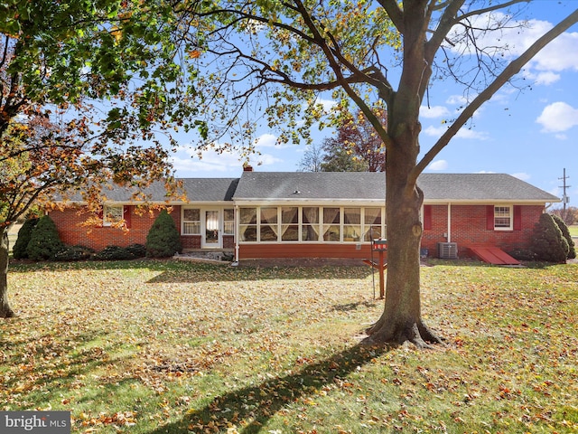 back of property with central AC, a sunroom, and a lawn