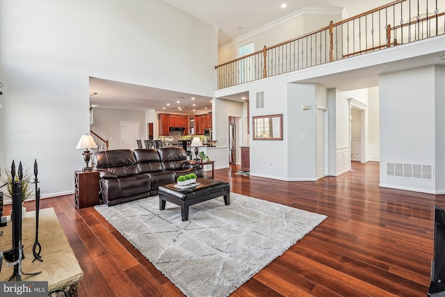 living room with a high ceiling, dark hardwood / wood-style flooring, and ornamental molding