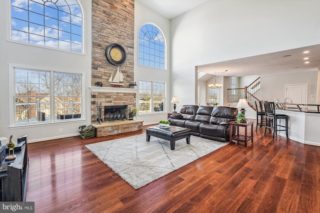 living room with a chandelier, a towering ceiling, hardwood / wood-style flooring, and a stone fireplace