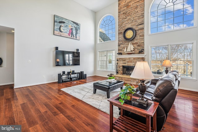 living room featuring a stone fireplace, a towering ceiling, and wood-type flooring