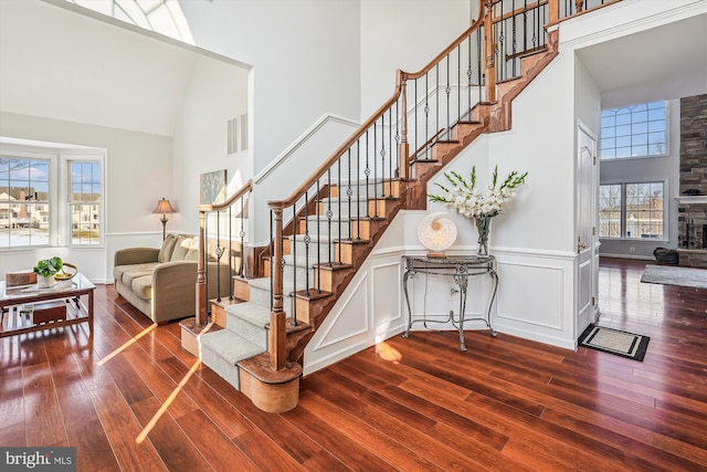 staircase with a stone fireplace, hardwood / wood-style floors, and high vaulted ceiling