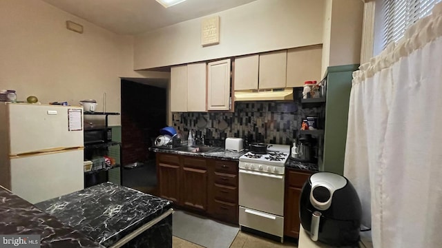 kitchen with sink, backsplash, gas stove, white fridge, and dark stone countertops