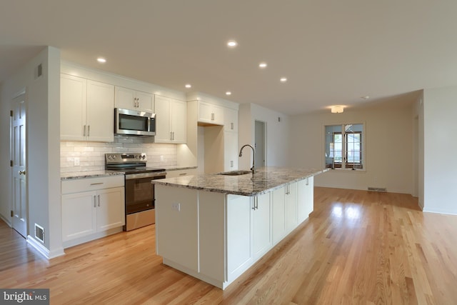 kitchen featuring white cabinets, a kitchen island with sink, stainless steel appliances, and stone countertops