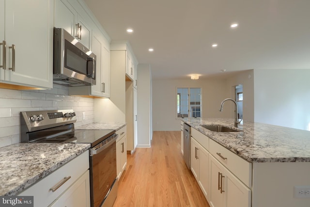 kitchen with light stone counters, appliances with stainless steel finishes, a kitchen island with sink, light hardwood / wood-style flooring, and sink