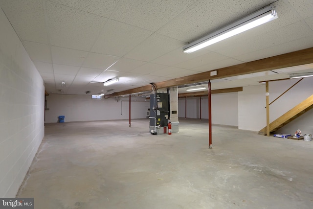 basement featuring a paneled ceiling and heating unit